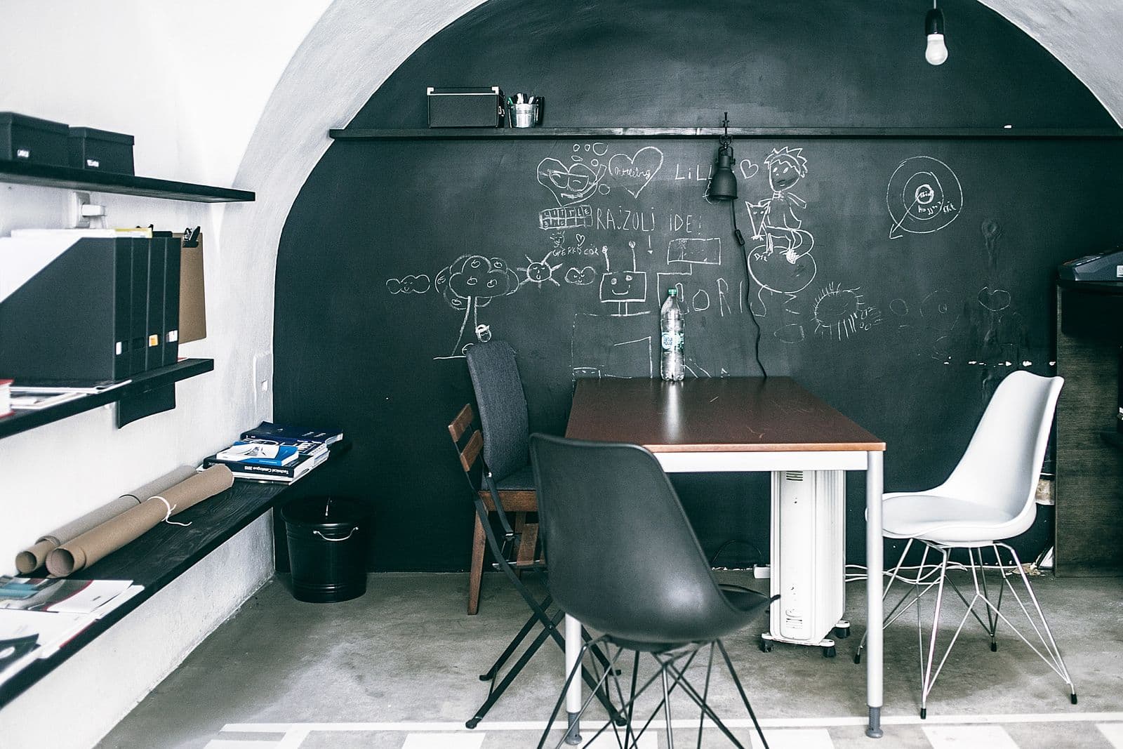 Office nook with a full chalkboard wall covered in chalk sketches behind a work table and chairs