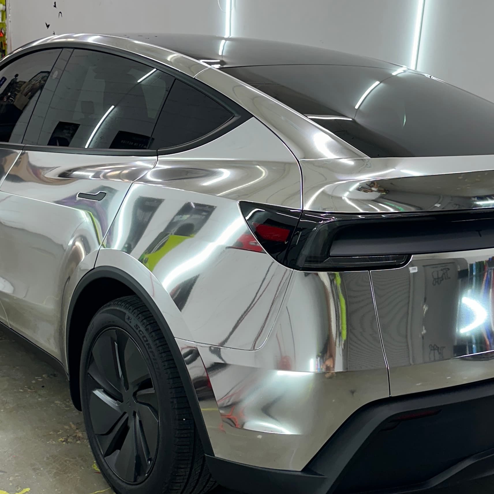 Freshly chrome-wrapped Tesla Model Y under inspection lights in the Wrap Trap shop