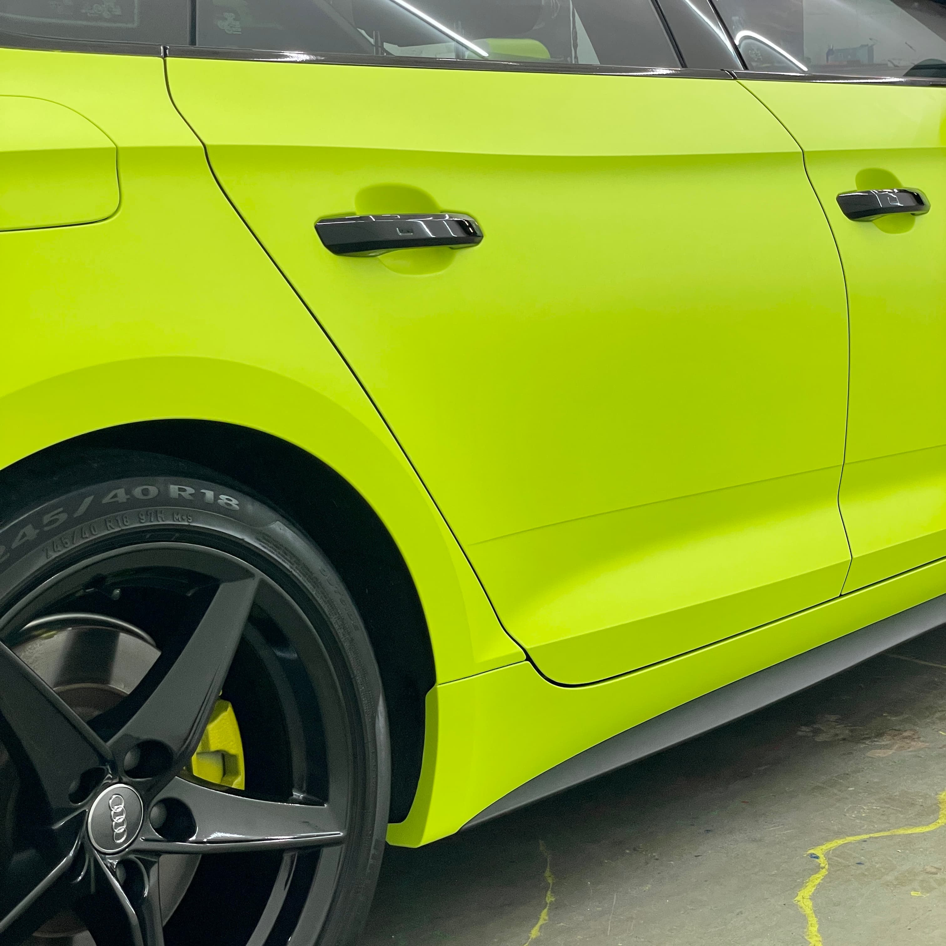 Side detail of an Audi wrapped in matte acid yellow with gloss-black door handles, blacked-out trim and black wheels.