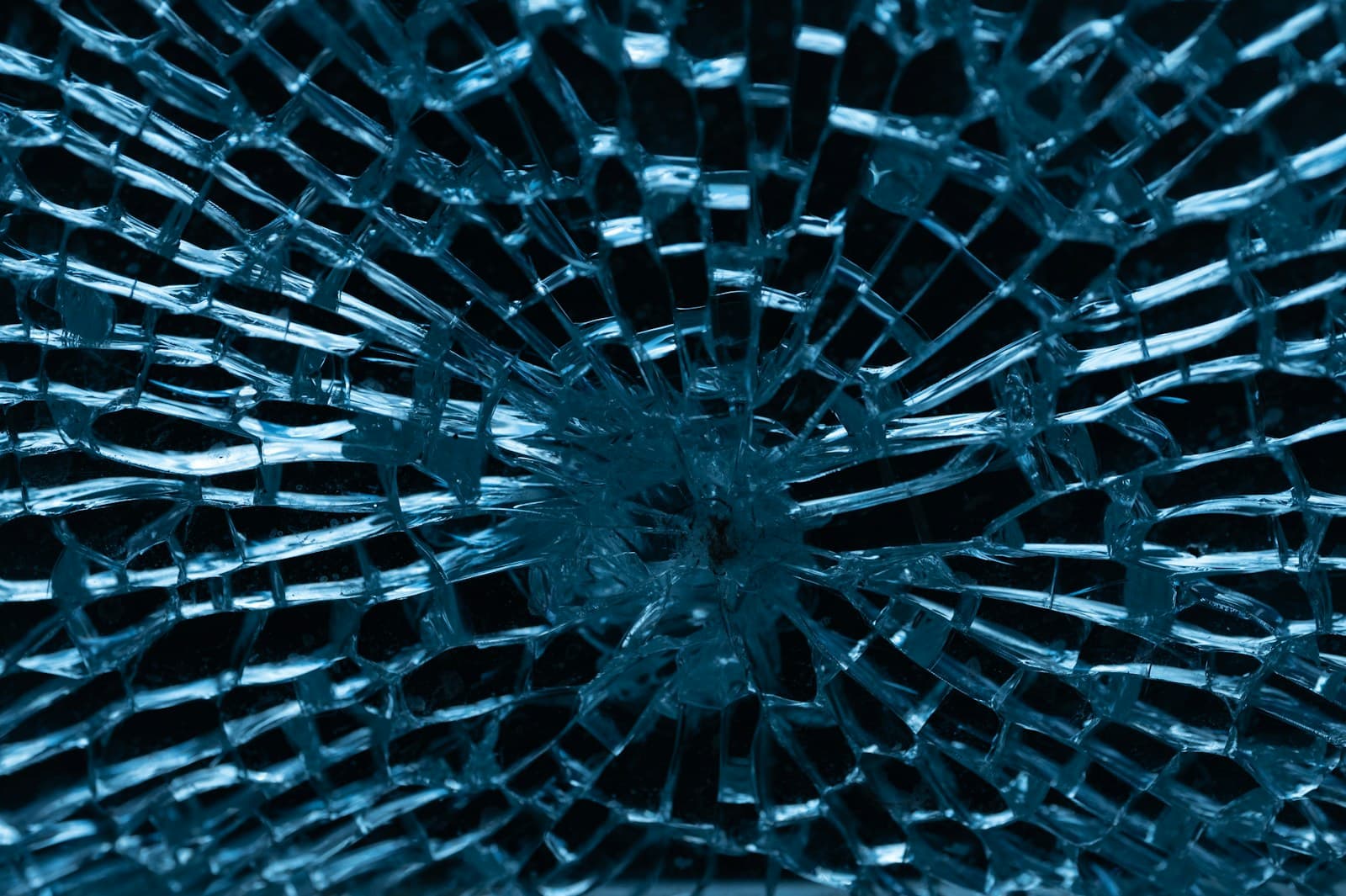 Shattered glass pane with a dense spiderweb crack pattern still holding together in one sheet