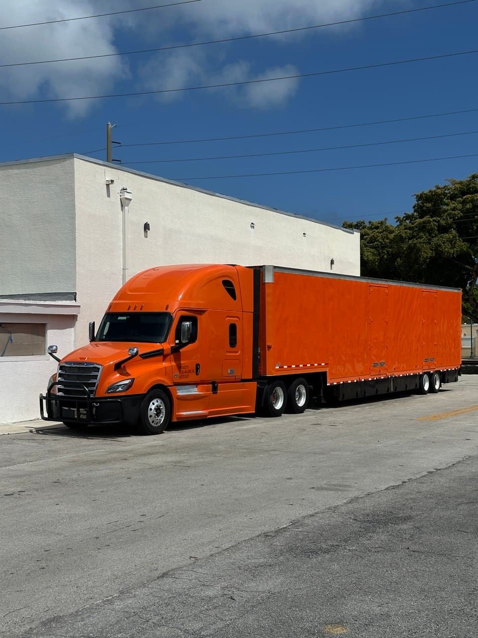 Semi tractor and 53-foot box trailer freshly wrapped in high-gloss orange, parked outside the shop.